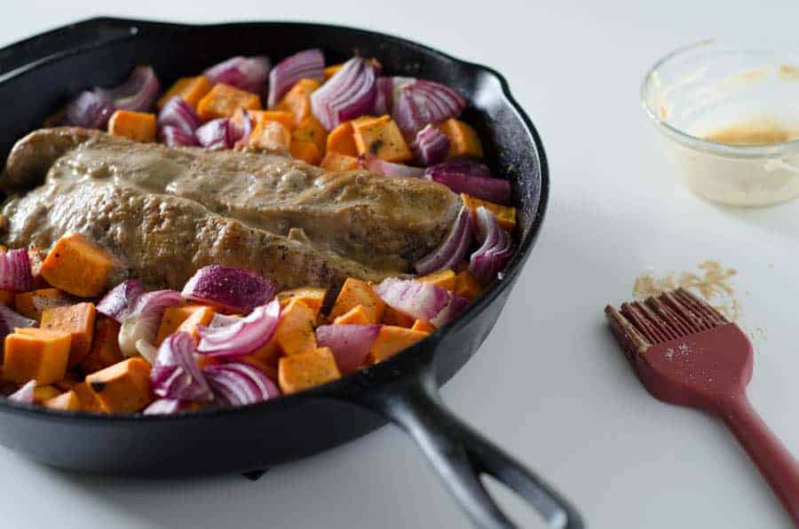 Whole30 pork tenderloin in cast iron skillet surrounded by sweet potato and red onion