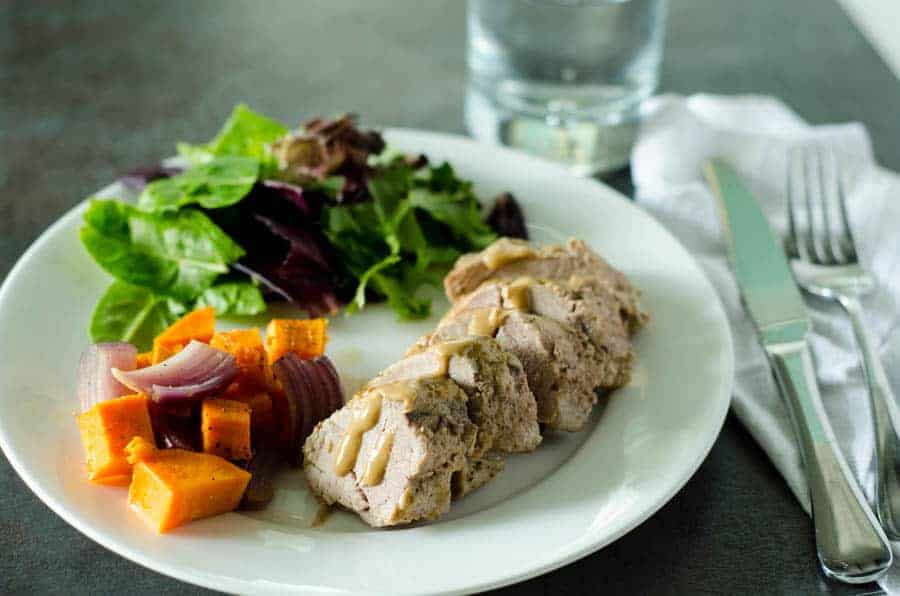 Whole30 pork tenderloin sliced on a white plate with veggies and mustard glaze drizzle