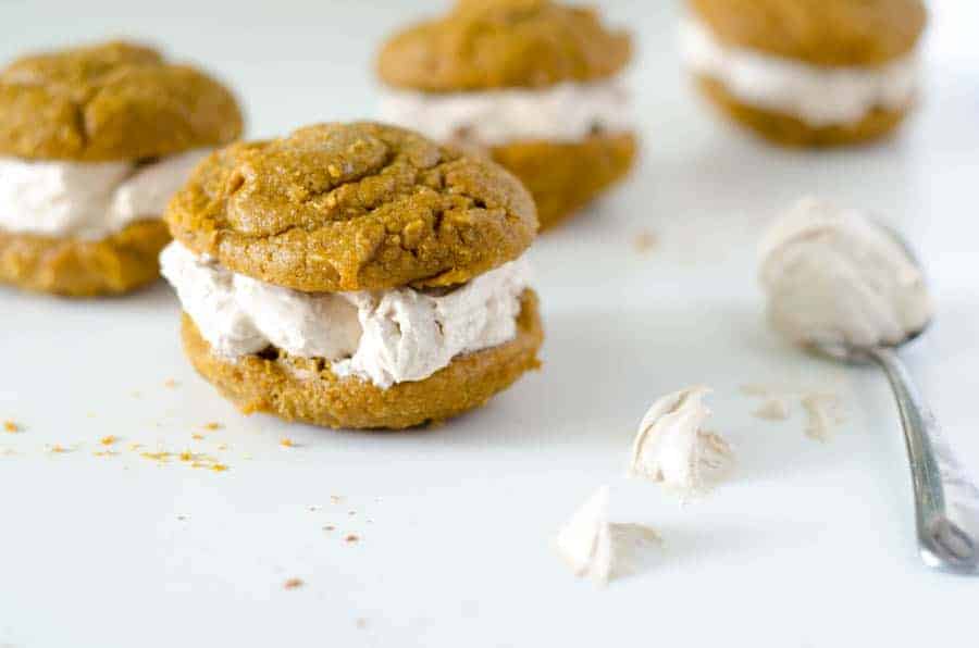 side view of pumpkin paleo whoopie pies with cinnamon cream filling with a spoon of cream filling next to it