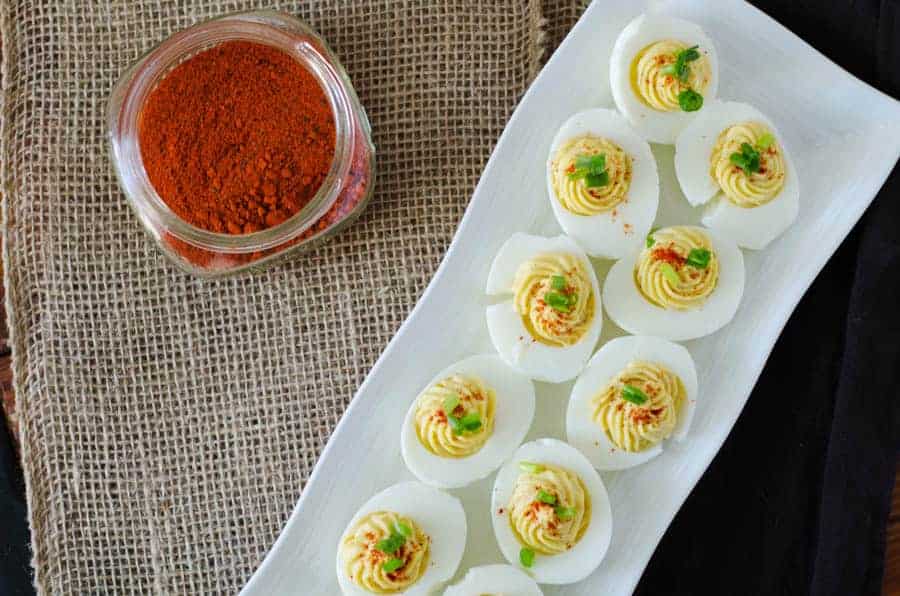 Overhead view of deviled eggs on a platter with a jar of paprika open next to it