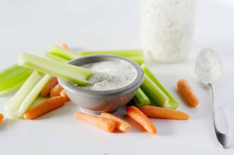 small bowl of ranch dressing surrounded by celery and carrots