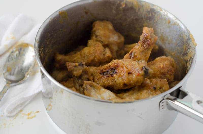 side view of a pot full of chicken wings tossed with sauce with a spoon in the background