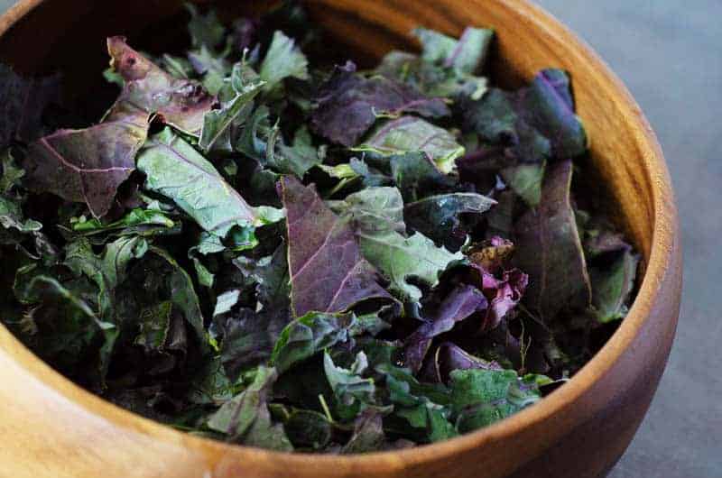 wooden salad bowl full of torn red russian kale
