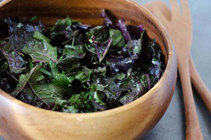 wooden salad bowl full of kale tossed with dressing with salad tongs on the side