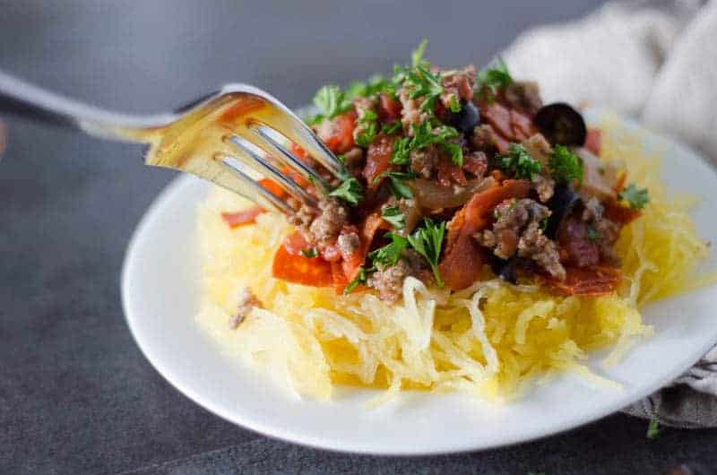 Close up side view of a white plate with paleo spaghetti squash recipe with fork digging in