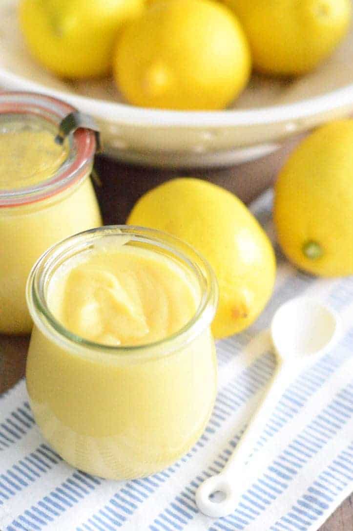 side overhead view of lemon curd in container with spoon and lemons