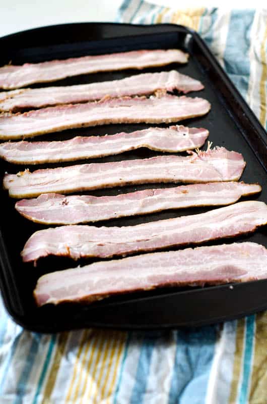 uncooked bacon laid out on a sheet pan