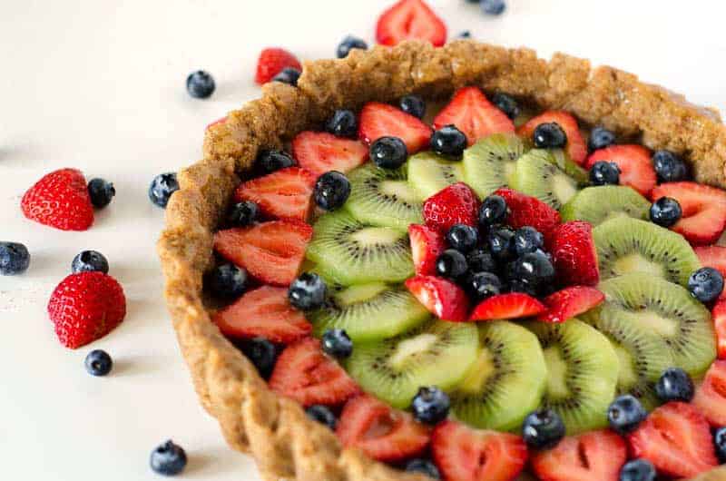 side view of a paleo fruit tart with mixed berries scattered nearby