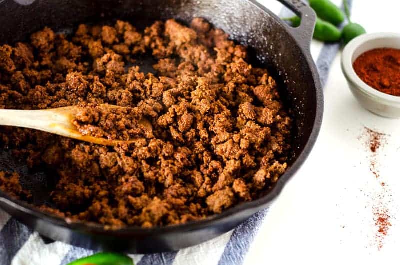 Paleo ground beef recipes showing cast iron skillet with ground beef cooking and wooden spoon