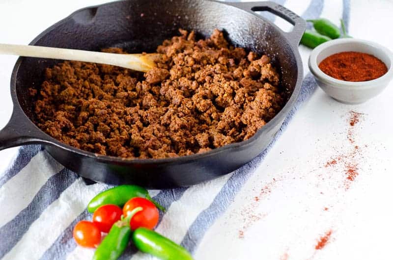 cast iron skillet full of homemade taco meat with a wooden spoon