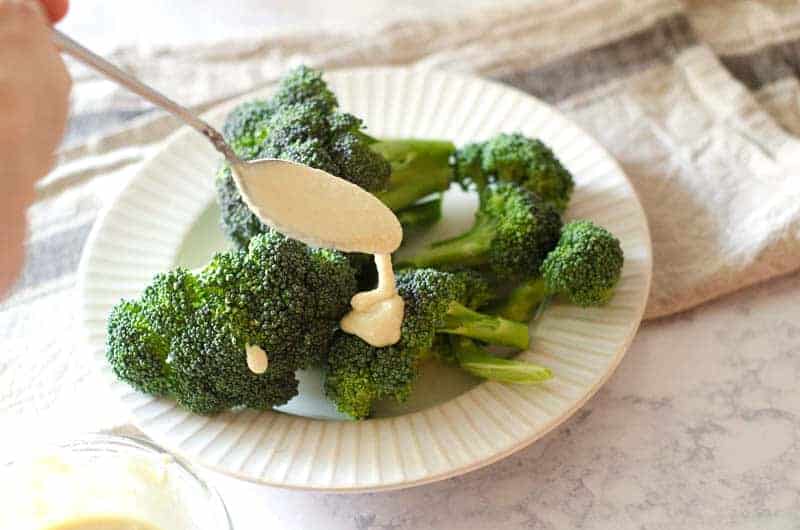 spoon drizzling dairy free cheese sauce over broccoli