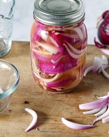 Side view of jar of pickled red onions on a cutting board