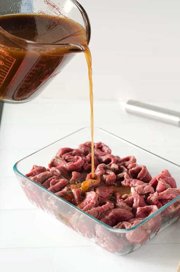 marinade being poured over meat for beef jerky