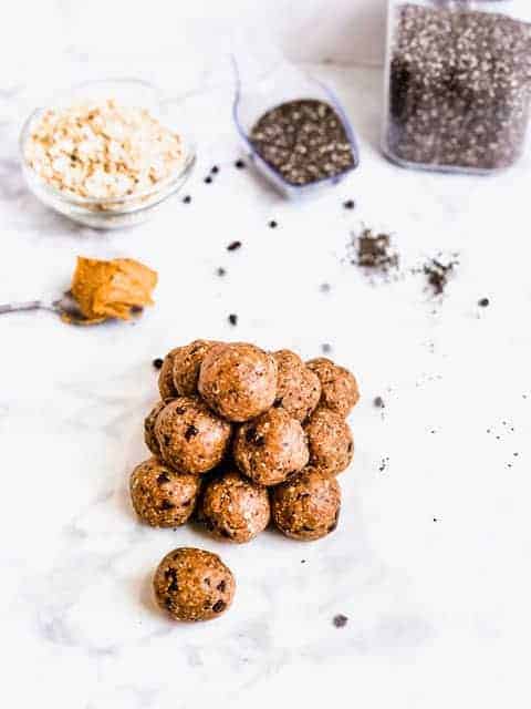 Pile of energy ball snacks on counter surrounded by oats, peanut butter and chia seeds
