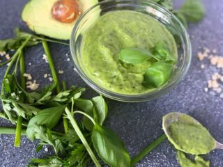 bowl of green goddess salad dressing surrounded by herbs and ingredients
