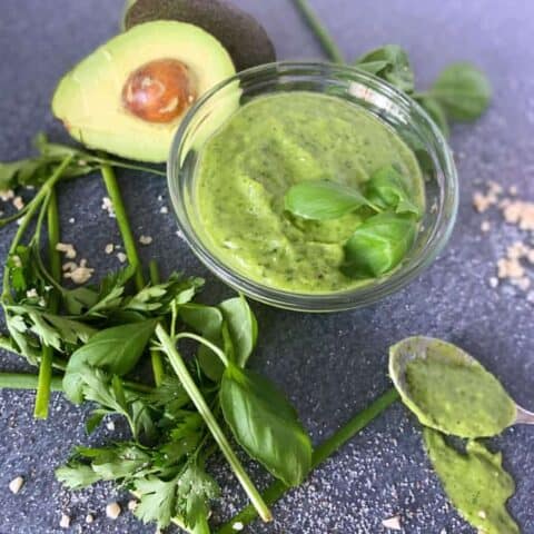 bowl of green goddess salad dressing surrounded by herbs and ingredients