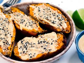 bowl of halved sweet potatoes topped with tahini spread and sesame seeds
