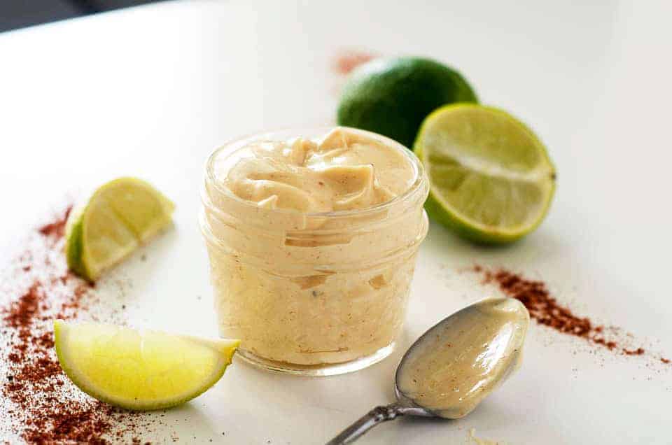 jar of chipotle lime mayo surrounded by chili powder, sliced limes, and a spoon