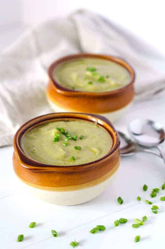 two bowls of dairy free broccoli soup on a table with spoons