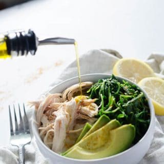 bowl of chicken, greens, and avocado being drizzled with olive oil