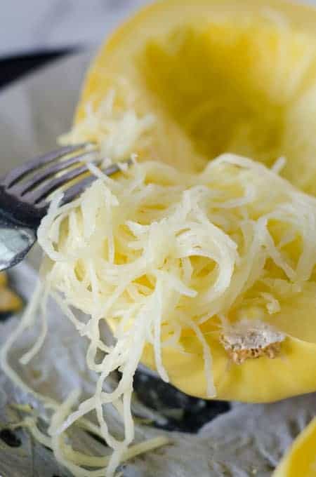 Close up view of a fork shredding the inside of a cooked spaghetti squash