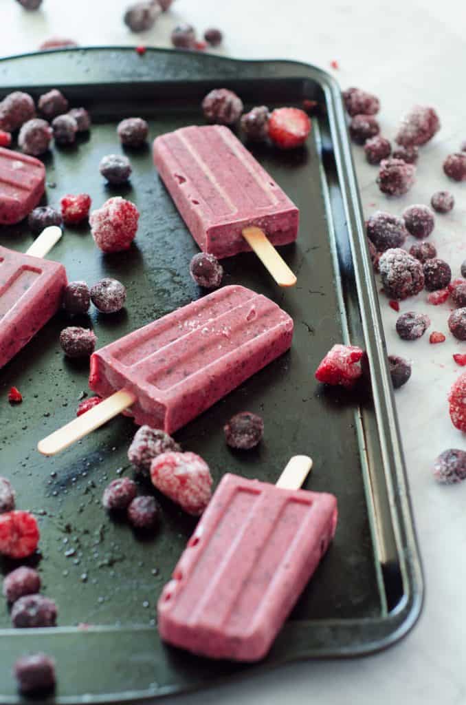 side view of berry popsicles on a baking sheet surrounded by frozen berries