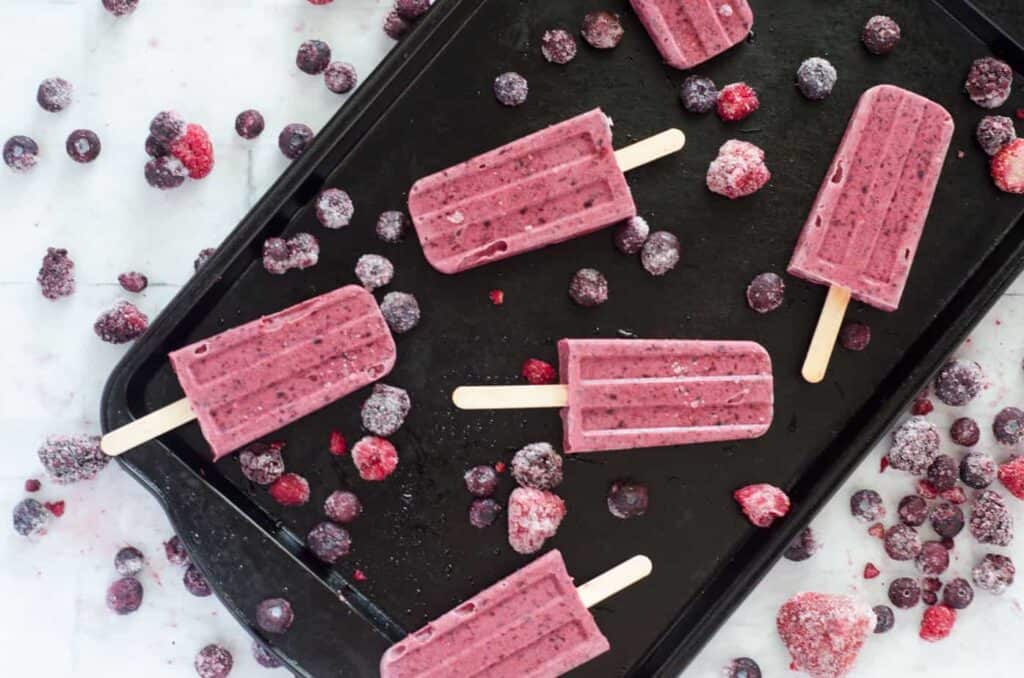 overhead view of berry coconut milk popsicles on a dark baking sheet surrounded by berries