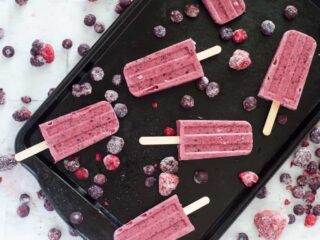 overhead view of berry popsicles on a dark baking sheet surrounded by berries