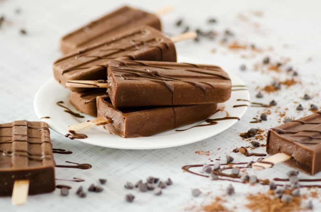 Side view of paleo chocolate popsicles on a plate drizzled with chocolate sauce
