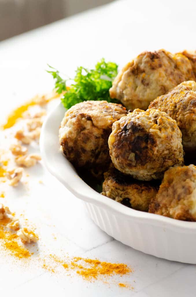 Close up image of Indian Meatballs in a serving dish garnished with parsley and surrounded by a sprinkle of walnuts and turmeric
