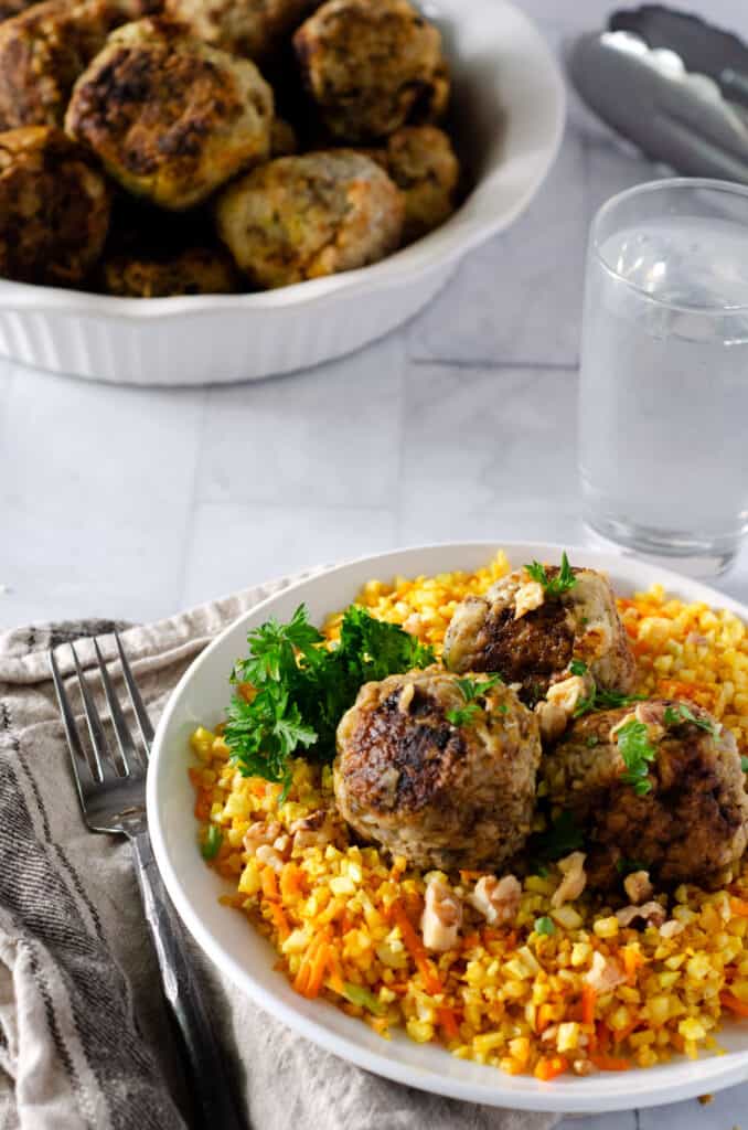 Indian meatballs on top of turmeric cauliflower rice with carrots and walnuts with a serving bowl in the background