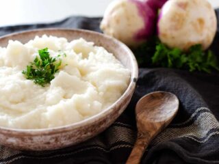 bowl of mashed turnips topped with parsley with a spoon and whole turnips in the background