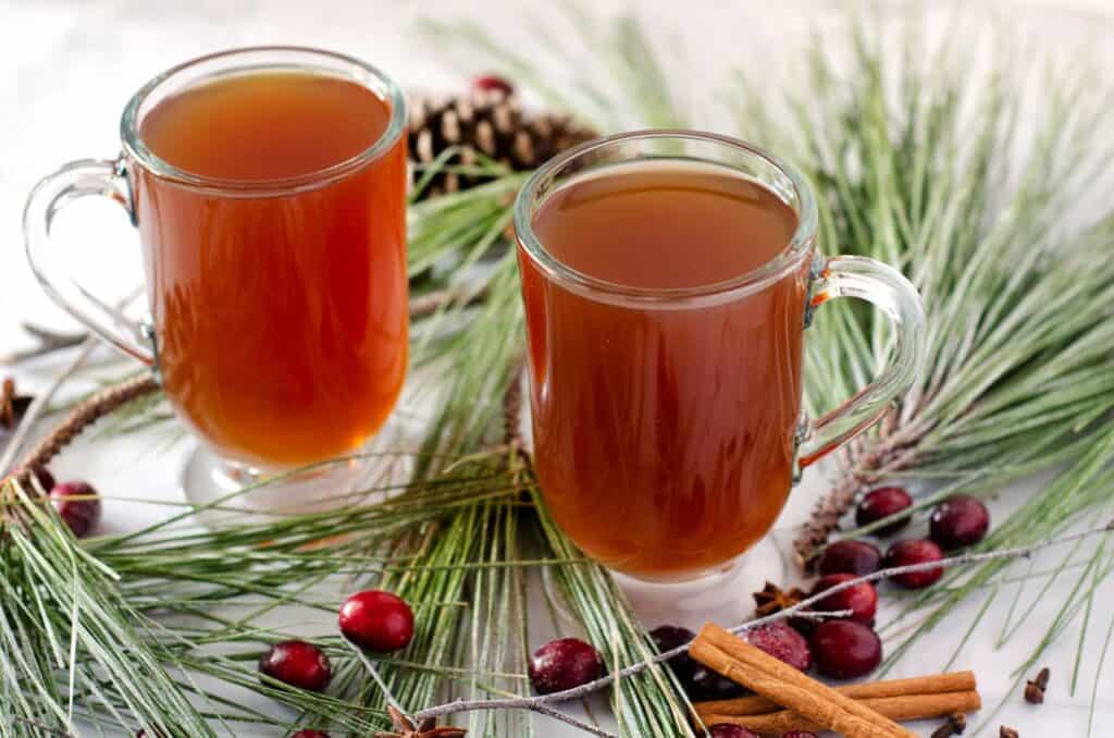 two glass mugs filled with snowblower holiday cocktail surrounded by pine branches, cranberries and cinnamon sticks