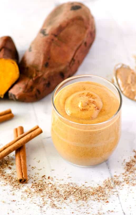 sweet potato smoothie in a clear glass surrounded by cinnamon sticks and flax meal