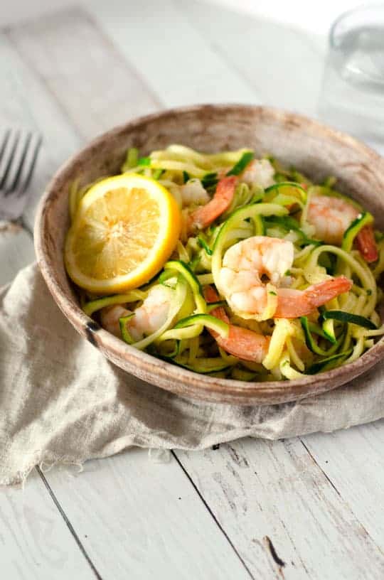 Paleo shrimp scampi in a bowl with a slice of lemon next to napkin and fork