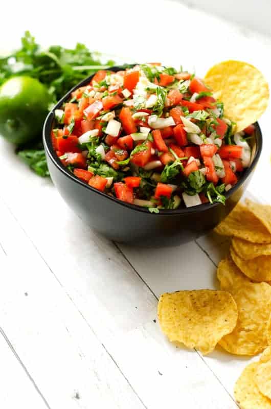 bowl of the best pico de gallo recipe surrounded by cilantro and limes