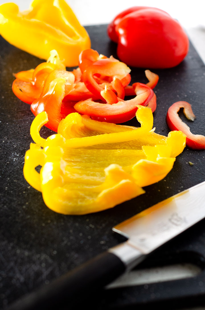 Close up of yellow and red bell peppers sliced on a black cutting board