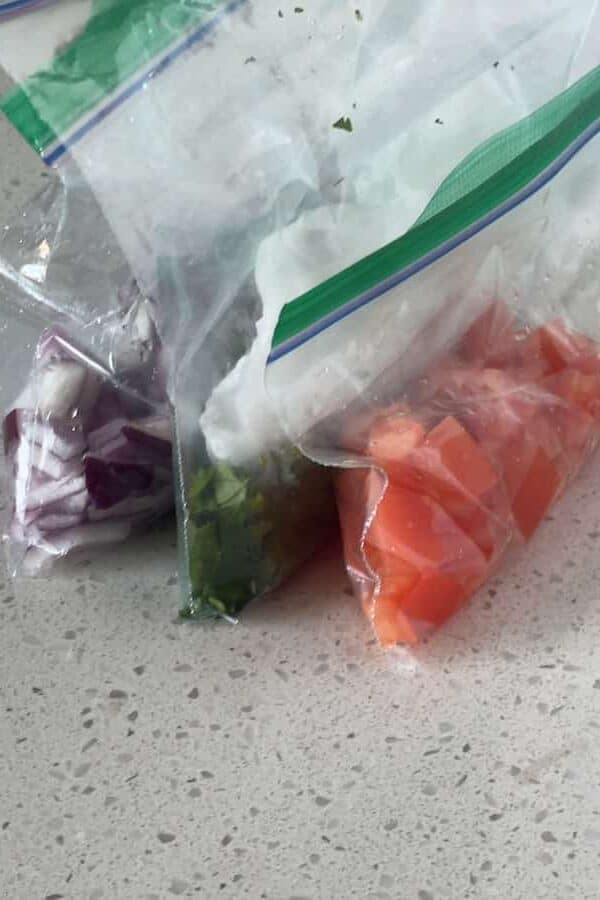 ziplock bags containing chopped red onion, chopped cilantro, and diced roma tomato on a countertop