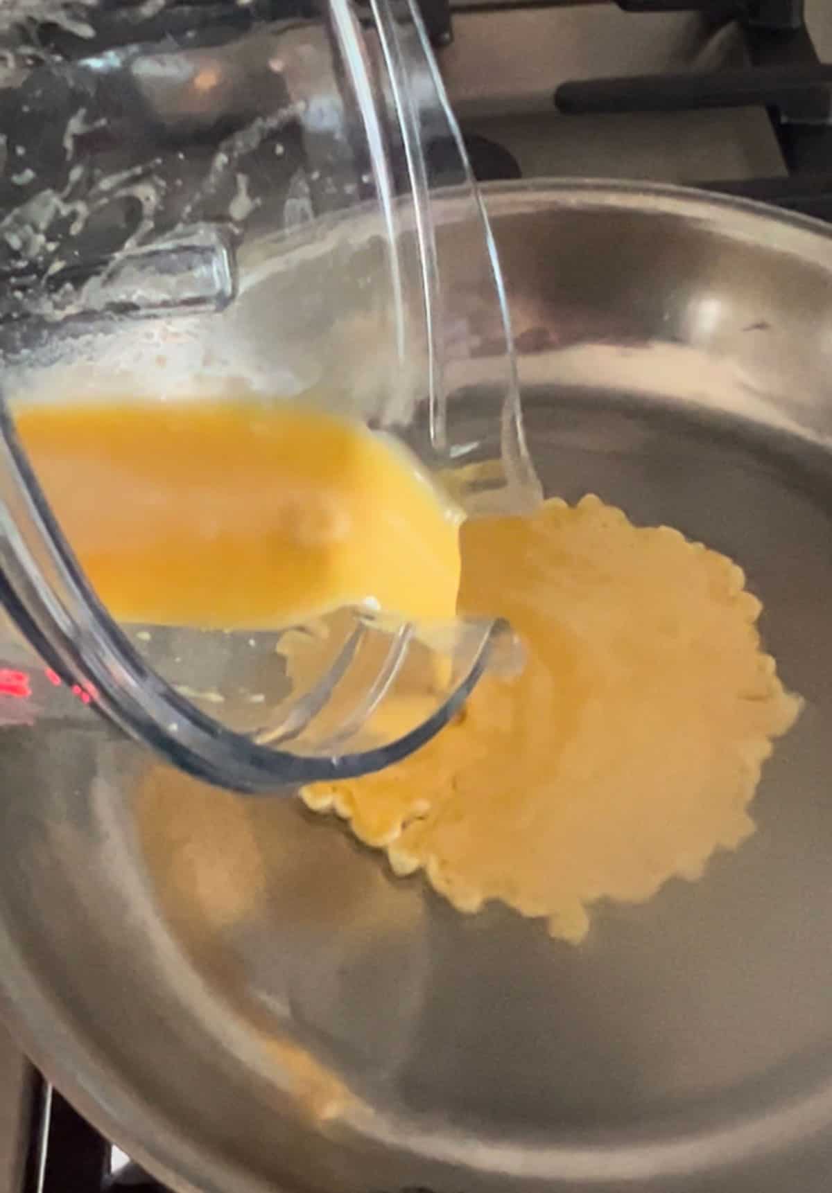 Egg batter being poured from a blender into a hot skillet on the stove