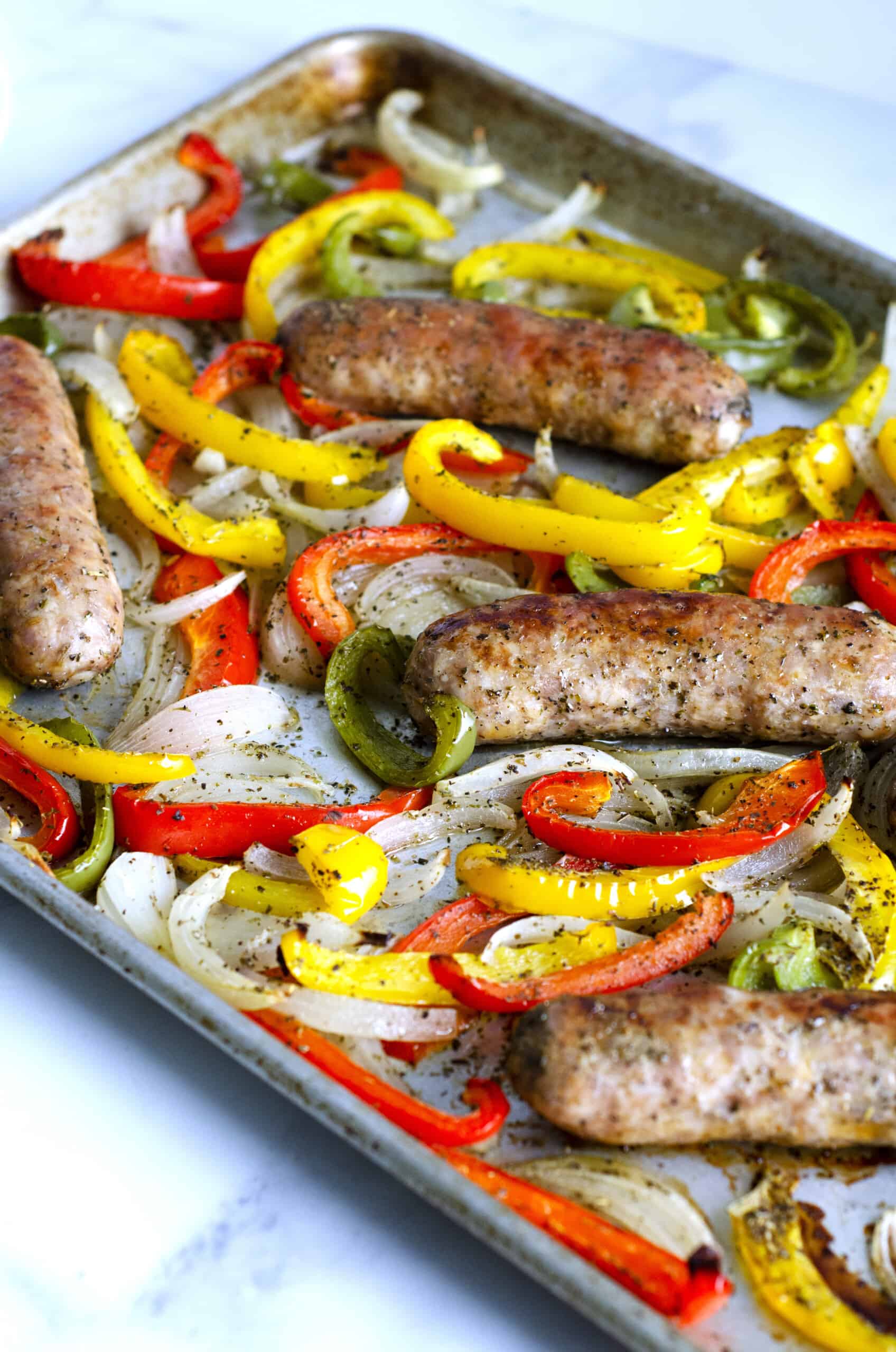 Close up of roasted sausage peppers and onions on a sheet pan