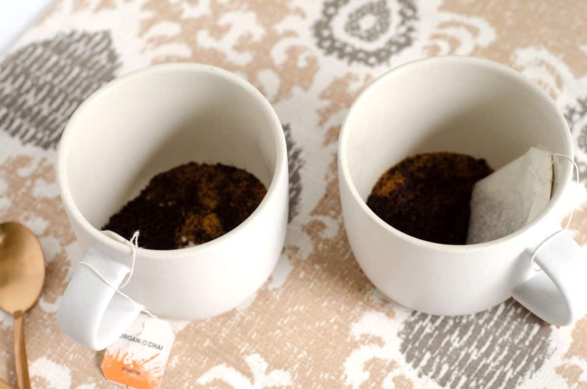¾ angle shot of tea bag, sugar, and espresso powder in a pair of mugs.
