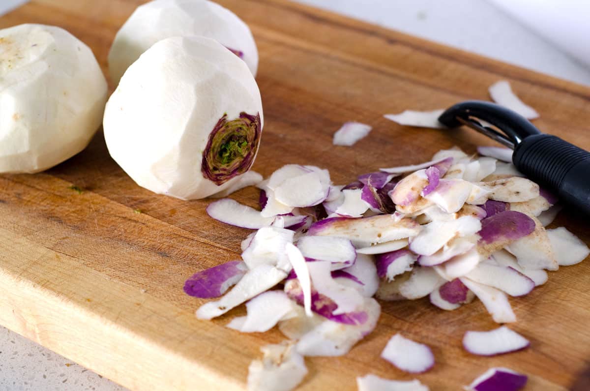 peeled turnips on a cutting board with peeler and peeled skin