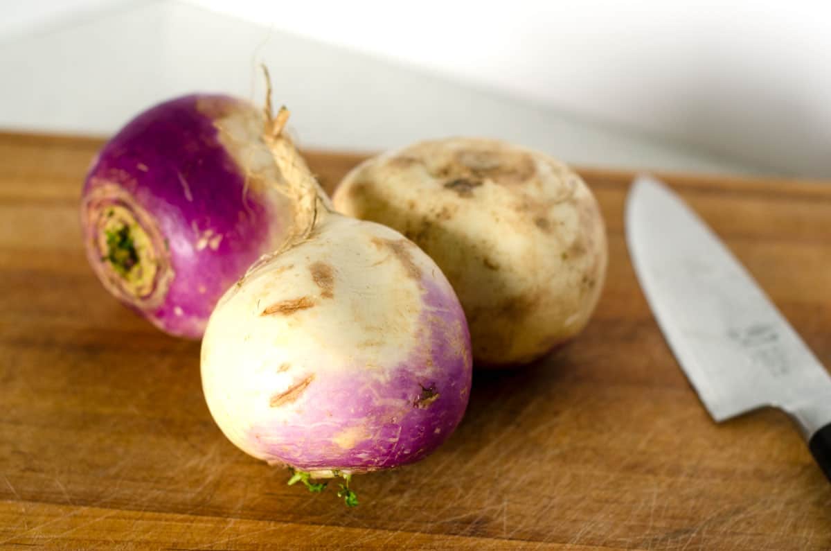 3 purple bottom turnips and a knife resting on a cutting board