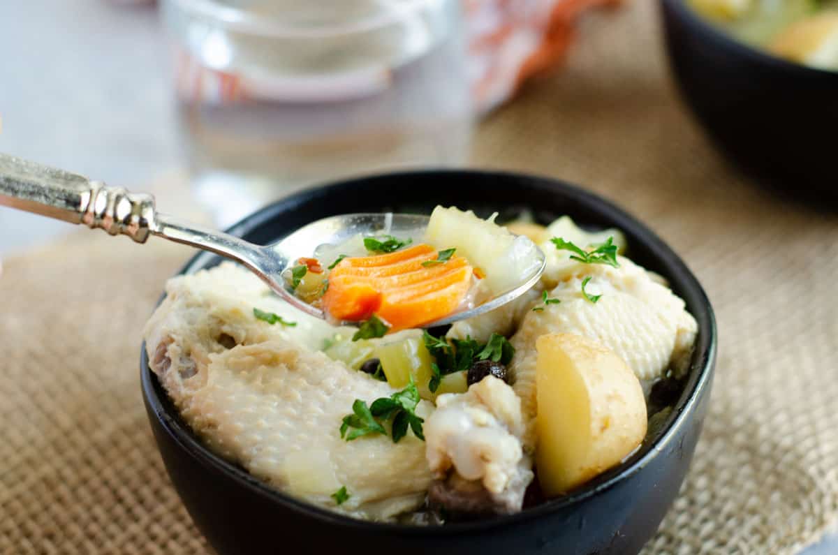 black bowl of bahamian chicken souse with spoonful of vegetables